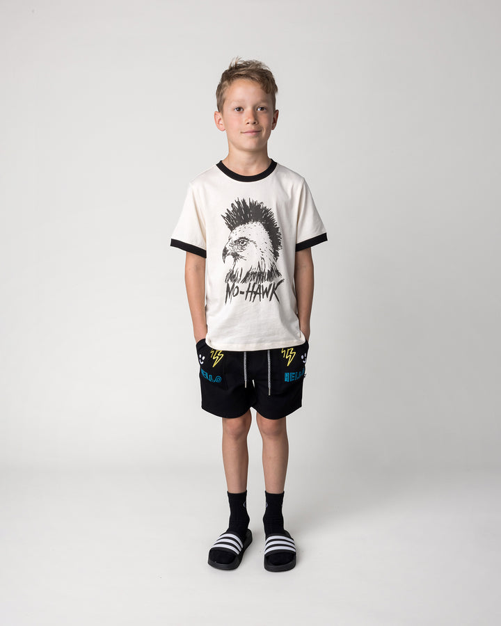 Kid wearing the Badges Short in black with the Mo-Hawk Tee in cream and black, front view