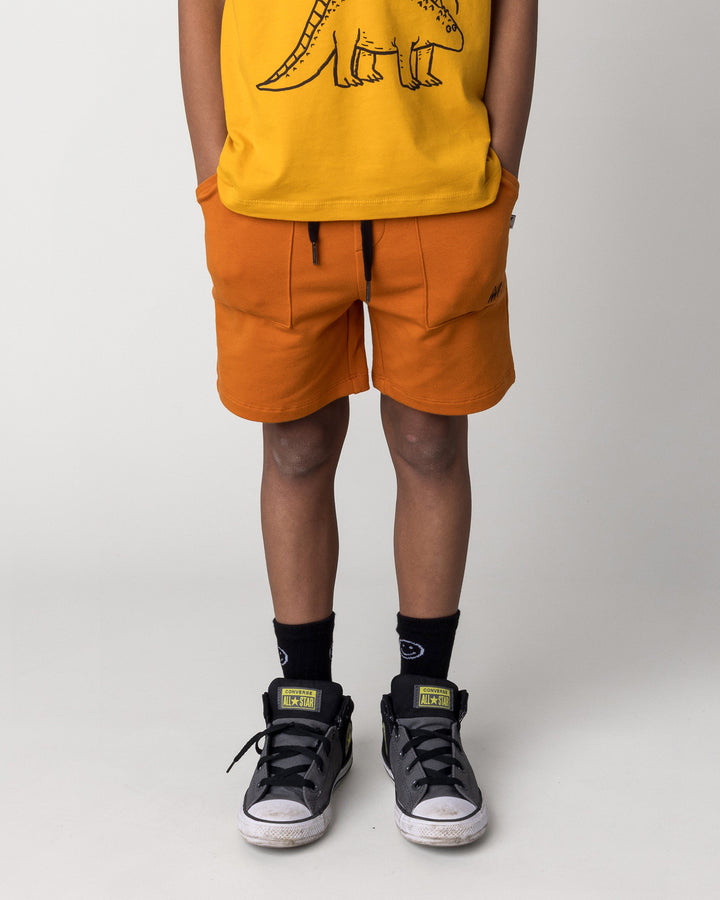Kid wearing the Track Short in burnt orange, front view close up