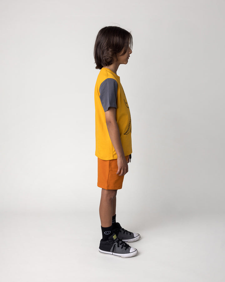 Kid wearing the Track Short in burnt orange with the Dino Ride Tee in mustard, grey and orange, side view