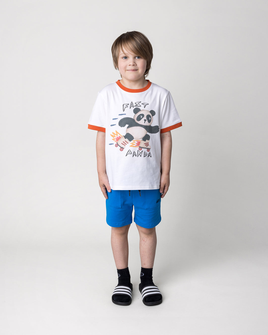 Kid wearing the Track Short in cobalt with the Fast Panda Tee in white and orange, front view