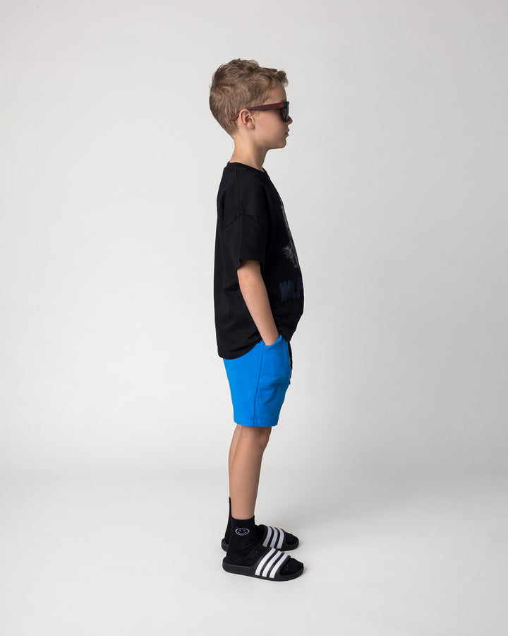 Kid wearing the Track Short in cobalt with the Wolfpack Tee in black, side view