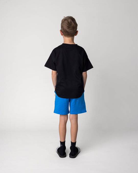 Kid wearing the Track Short in cobalt with the Wolfpack Tee in black, back view