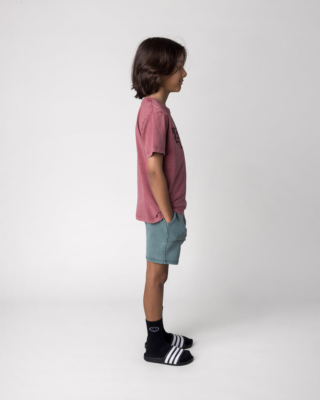 Kid wearing the Blasted Track Short in forest wash with the Hello Bat Tee in burnt red wash, side view
