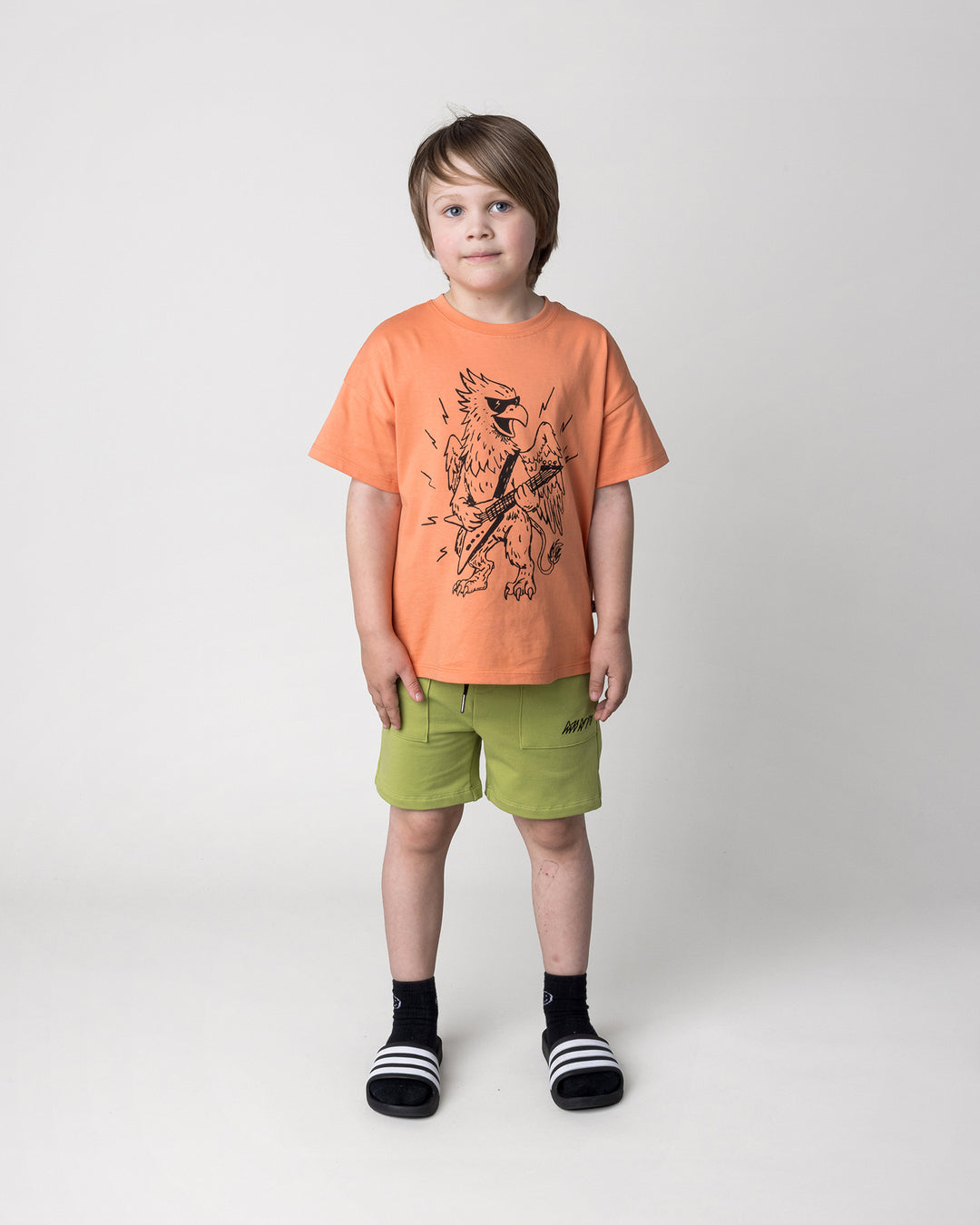 Kid wearing the Track Short in lime with the Rock Griffin Tee in light orange, front view