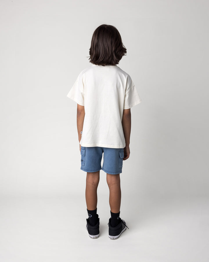 Kid wearing the Blasted Deluxe Cargo Short in midnight wash with the Cool Crew Tee in cream, back view