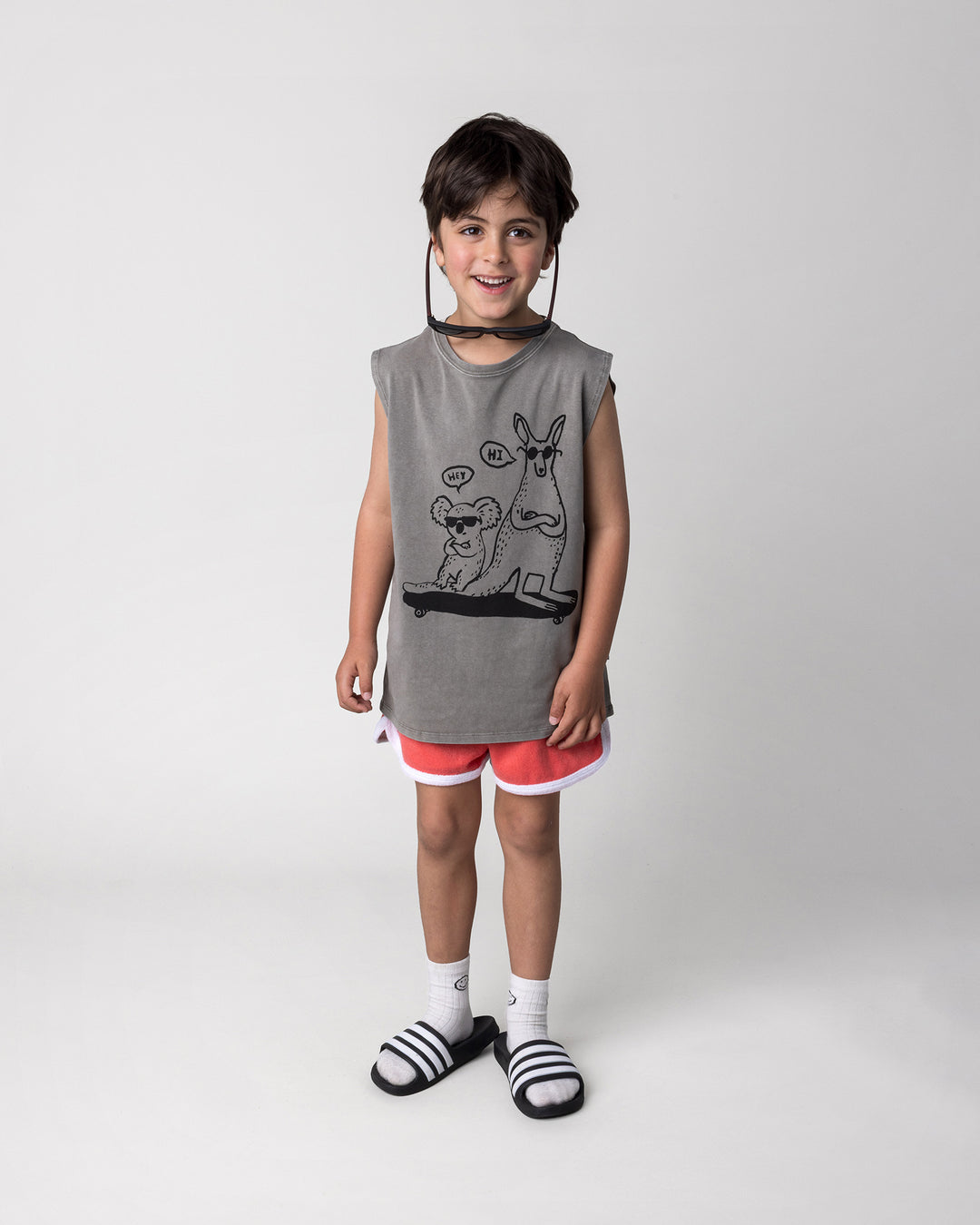 Kid wearing the Chill Mates Sleeveless Tee in grey wash with the Track Star Short in tangerine, front view