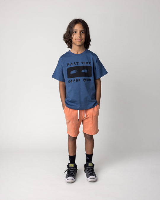 Kid wearing the Blasted Panel Short in orange wash with the Part Time Super Hero Tee in midnight, front view