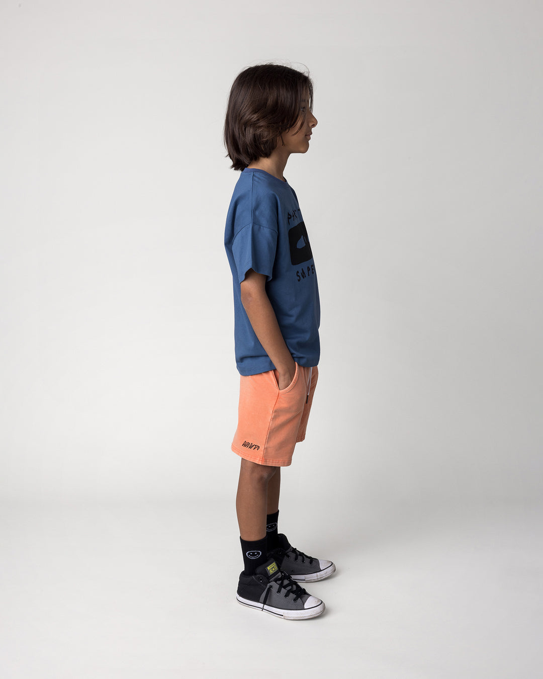 Kid wearing the Blasted Panel Short in orange wash with the Part Time Super Hero Tee in midnight, side view