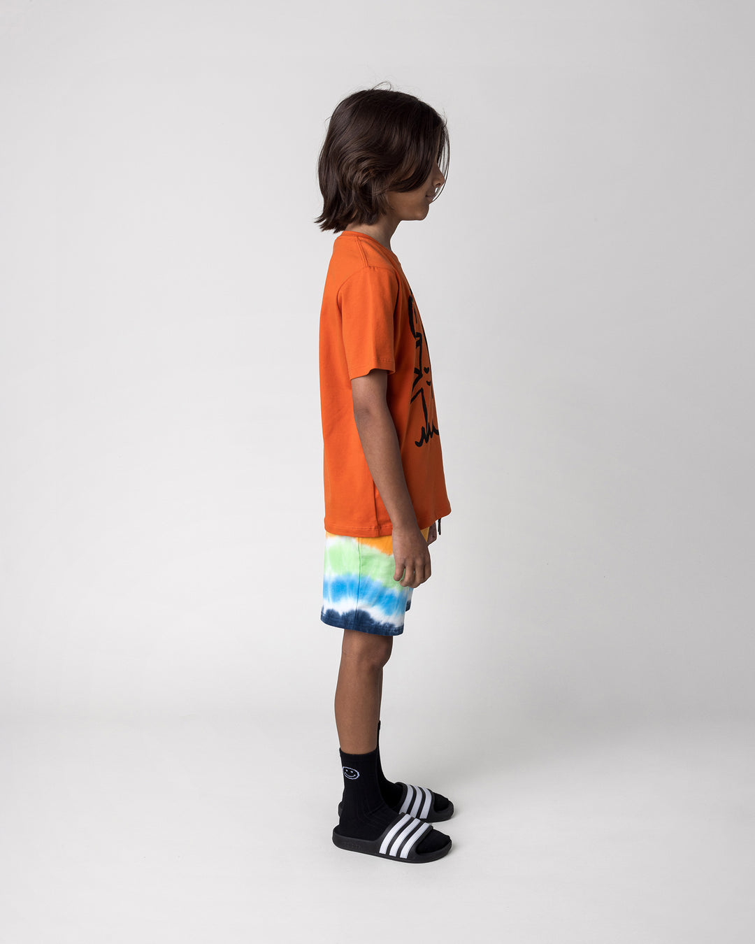 Kid wearing the Airwaves Short in navy with the Hi Hammerhead Tee in orange, side view