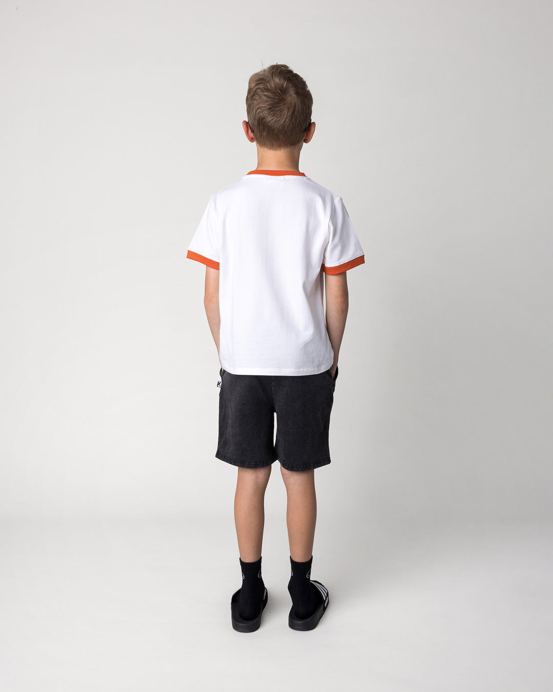 Kid wearing the Blasted Icon Short in black wash with the Fast Panda Tee in white and orange, back view