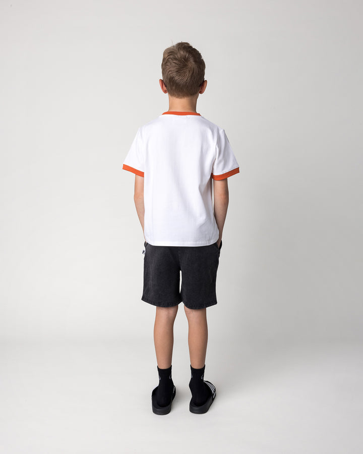 Kid wearing the Blasted Icon Short in black wash with the Fast Panda Tee in white and orange, back view