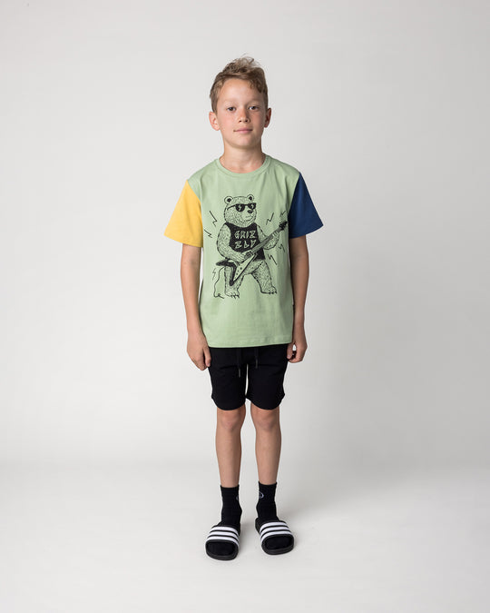 Kid wearing the Hero Short in black with the Grizzly Tee in sage, yellow and midnight, front view