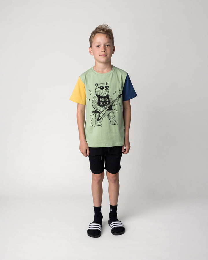Kid wearing the Hero Short in black with the Grizzly Tee in sage, yellow and midnight, front view