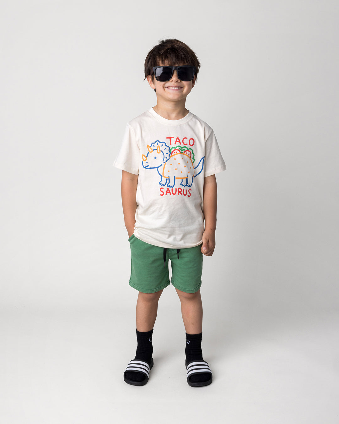 Kid wearing the Blasted Icon Short in turf wash with the Taco Saurus Tee in cream, front view
