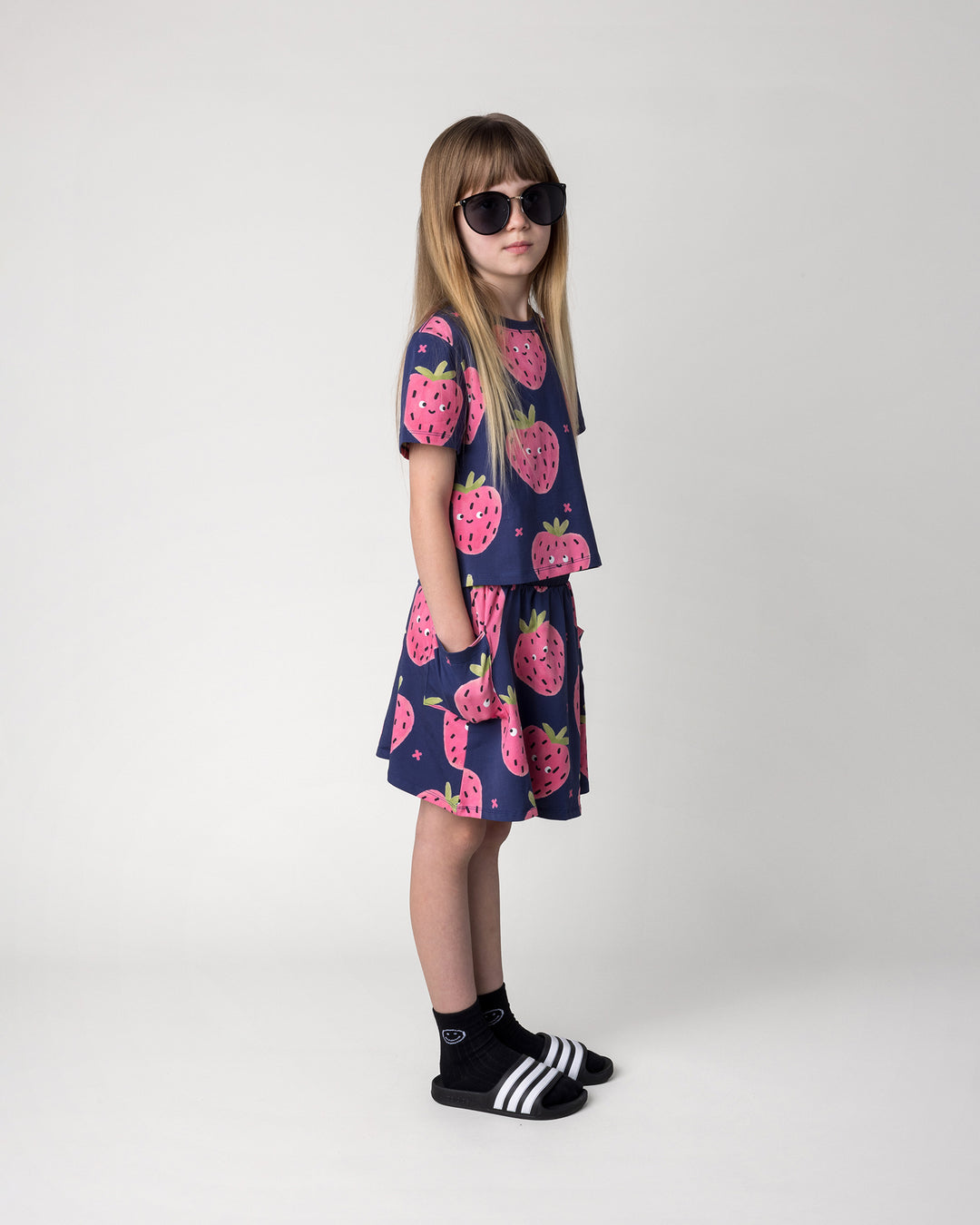 Kid wearing the Happy Strawberry Cropped Tee in turquoise with the Happy Strawberry Skirt in turquoise, side view