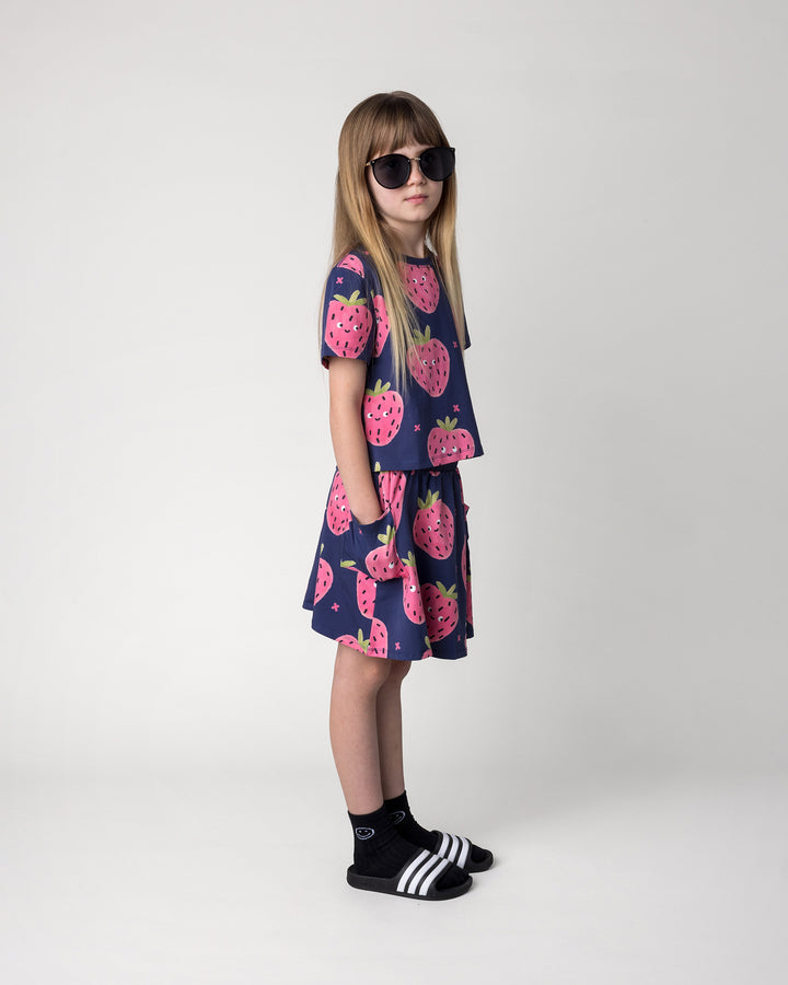 Kid wearing the Happy Strawberry Cropped Tee in turquoise with the Happy Strawberry Skirt in turquoise, side view