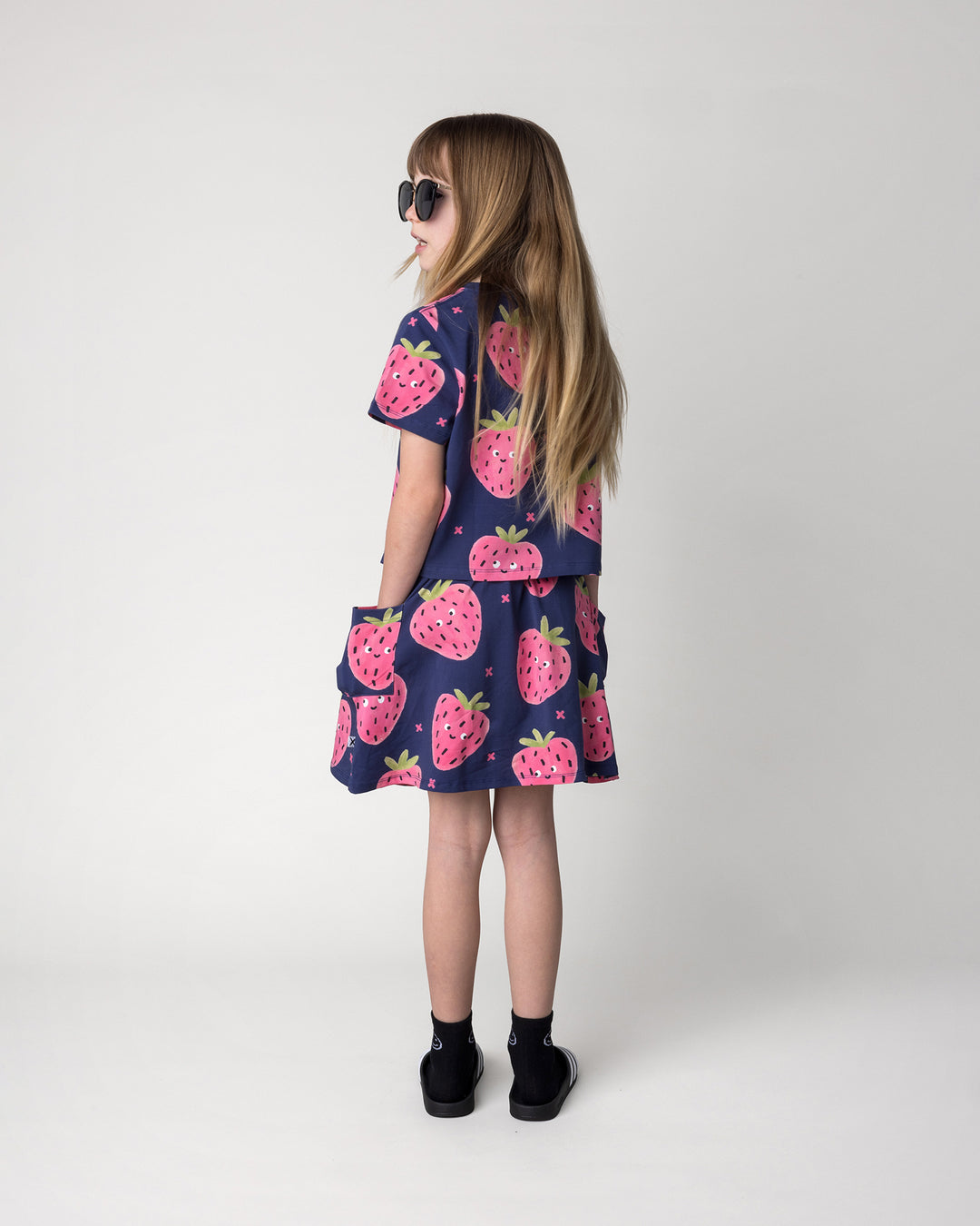 Kid wearing the Happy Strawberry Cropped Tee in turquoise with the Happy Strawberry Skirt in turquoise, back view