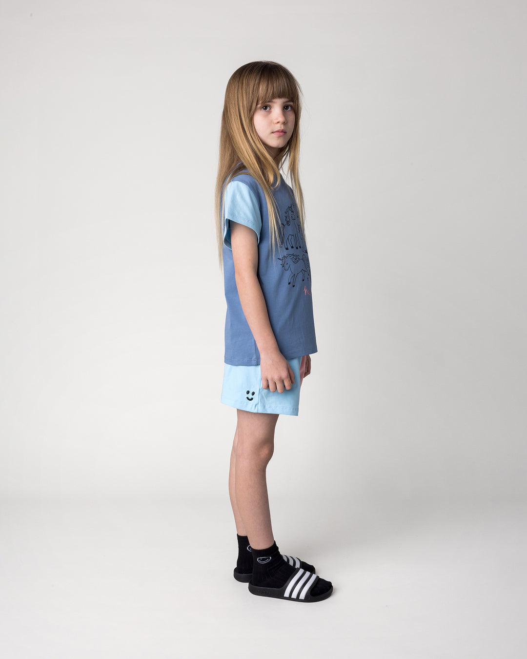 Kid wearing the Two Tone Short in light blue and pink with the Hello Unicorns Tee in mid blue, light blue and pink, side view