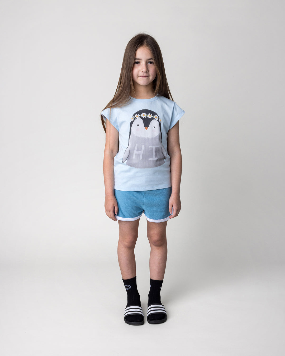 Kid wearing the Flower Penguin Tee in light blue with the Track Star Short in ocean, front view