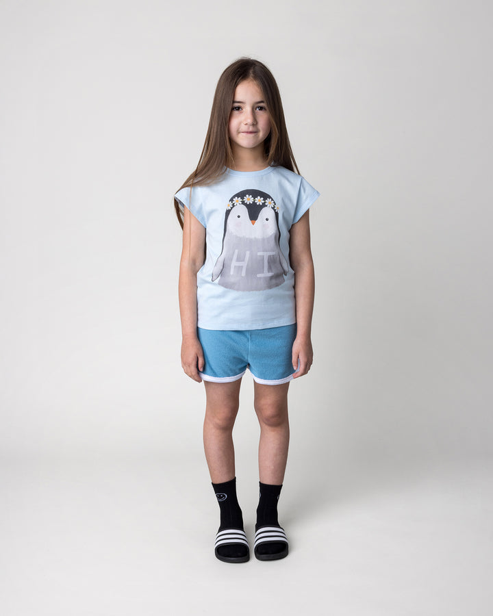 Kid wearing the Flower Penguin Tee in light blue with the Track Star Short in ocean, front view