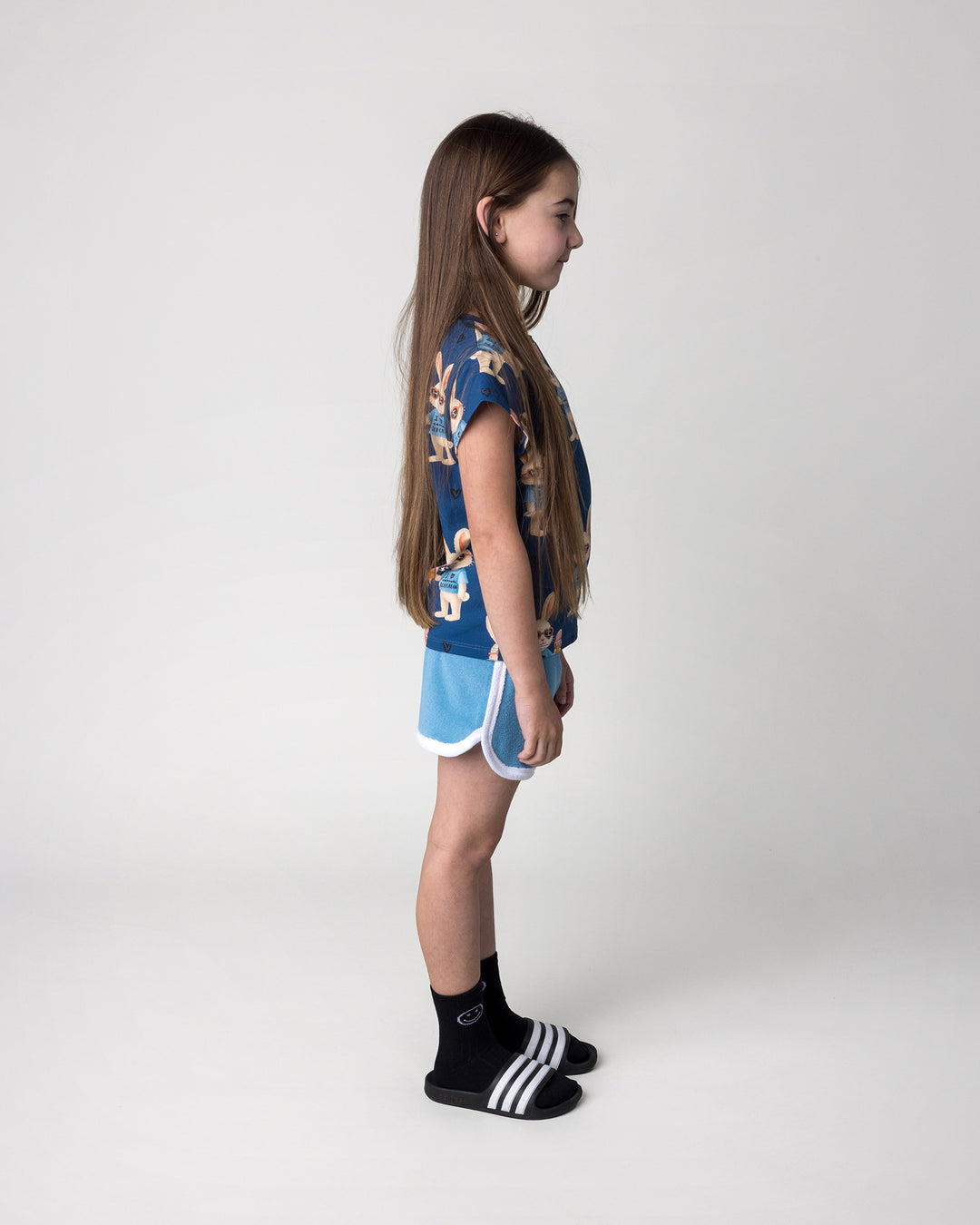 Kid wearing the Icecream Bunny Tee in blue with the Track Star Short in ocean, side view