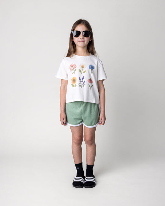 Kid wearing the Track Star Short in sage with the Flower Friends Cropped Tee in white, front view