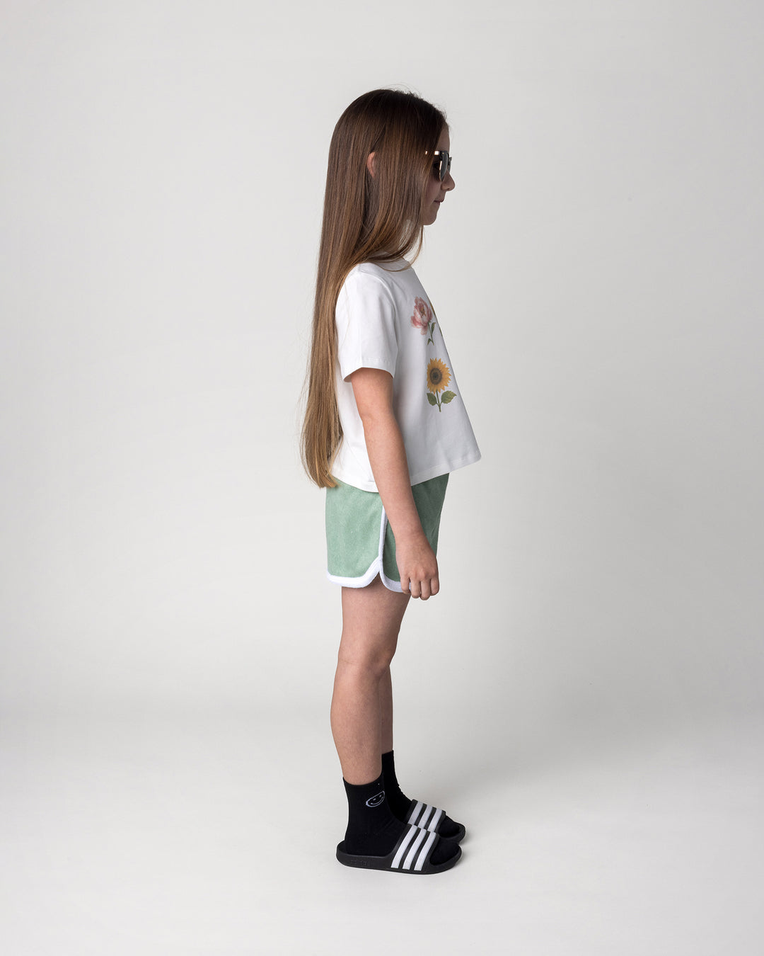 Kid wearing the Track Star Short in sage with the Flower Friends Cropped Tee in white, side view