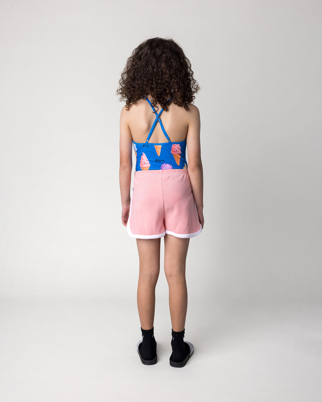 Kid wearing the Track Star Short in pink with the Happy Icecreams Swimsuit in bright blue, back view
