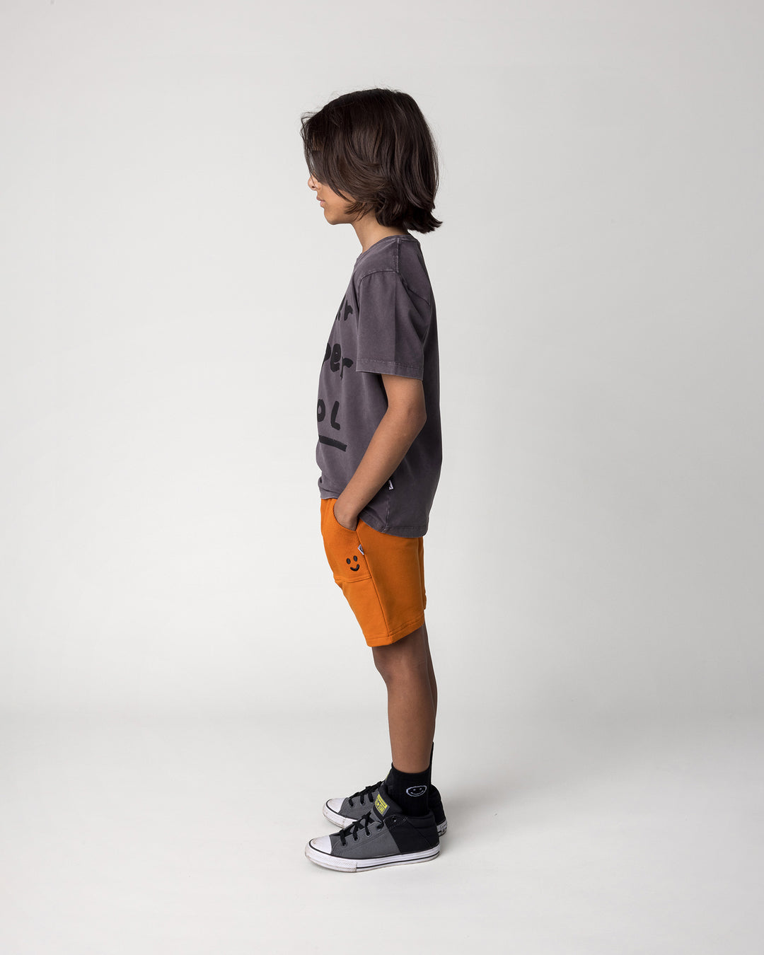 Kid wearing the Rib Pocket Short in burnt orange with the Super Duper Cool Tee in black wash, side view