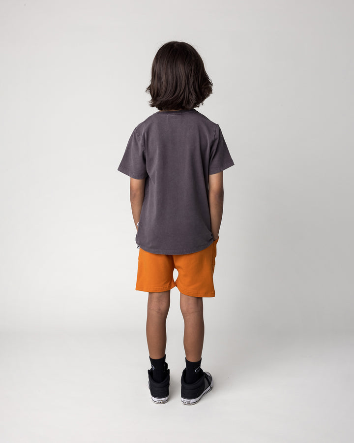 Kid wearing the Rib Pocket Short in burnt orange with the Super Duper Cool Tee in black wash, back view