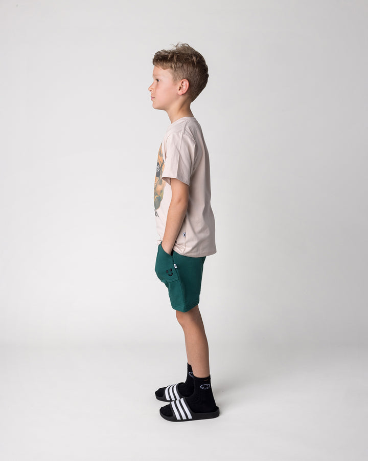 Kid wearing the Rib Pocket Short in kelly green with the Headphones Tiger Tee in stone, side view