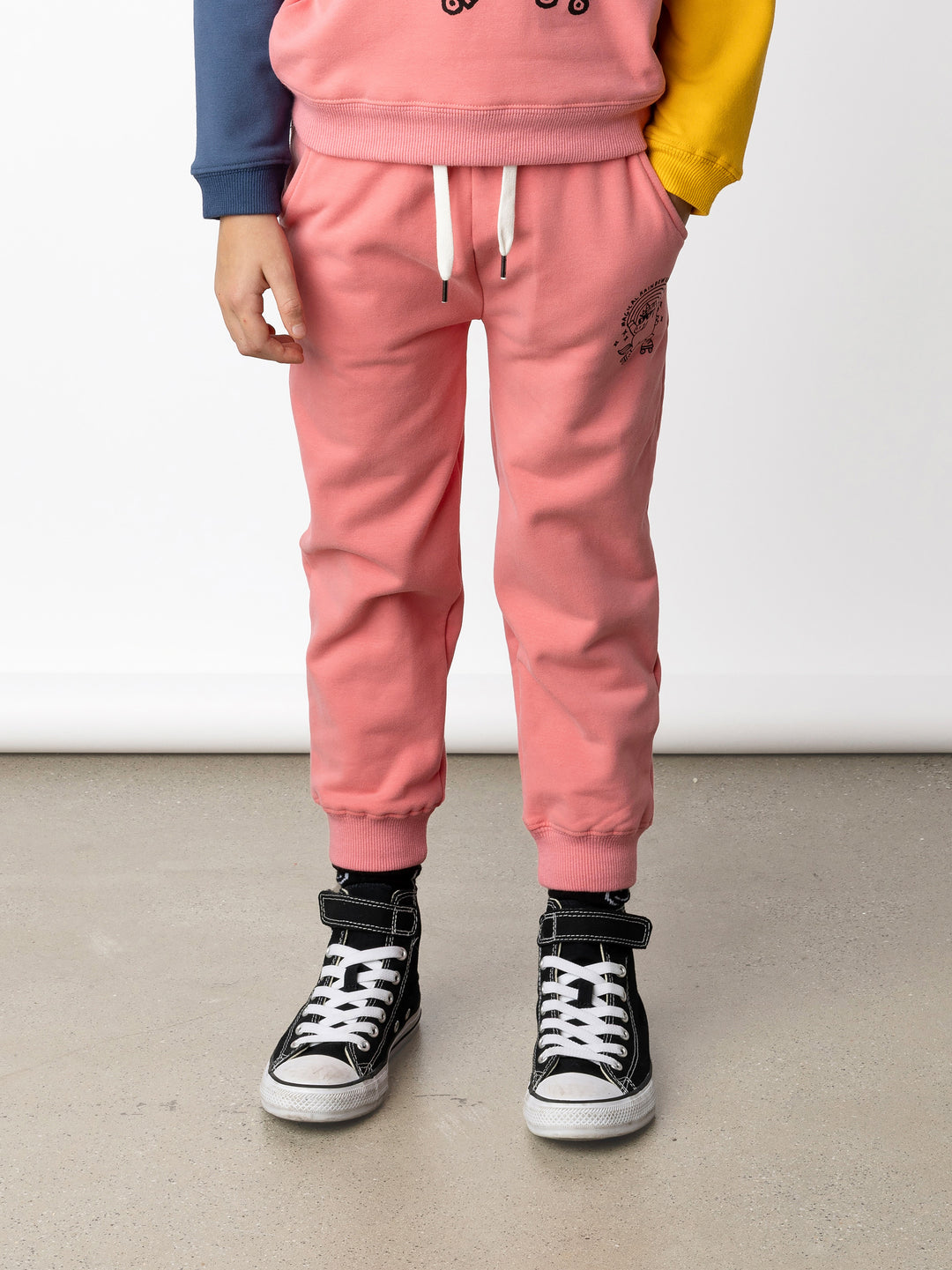 Minti kids clothing. Relaxed fit trackies with cosy side pockets, elasticated waistband, shoelace cord and 2x2 Rib cuffs. Small Magical Rainbow Unicorn print on the front. 330 Gram // Brushed Inside // 95% Cotton // 5% Elastane.