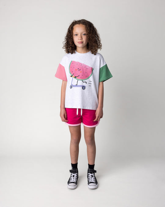 Kid wearing the Sprint Short in crimson and pink with the Scooting Watermelon Tee in white marle, candy and green, front view