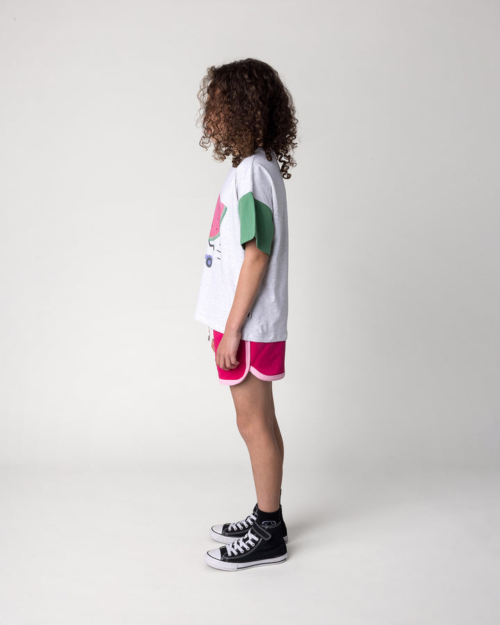 Kid wearing the Sprint Short in crimson and pink with the Scooting Watermelon Tee in white marle, candy and green, side view