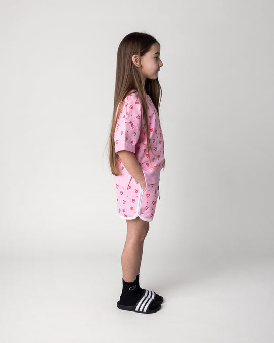 Kid wearing the Hearts Short in pink and white with the Hearts Short Sleeve Crew in pink, side view