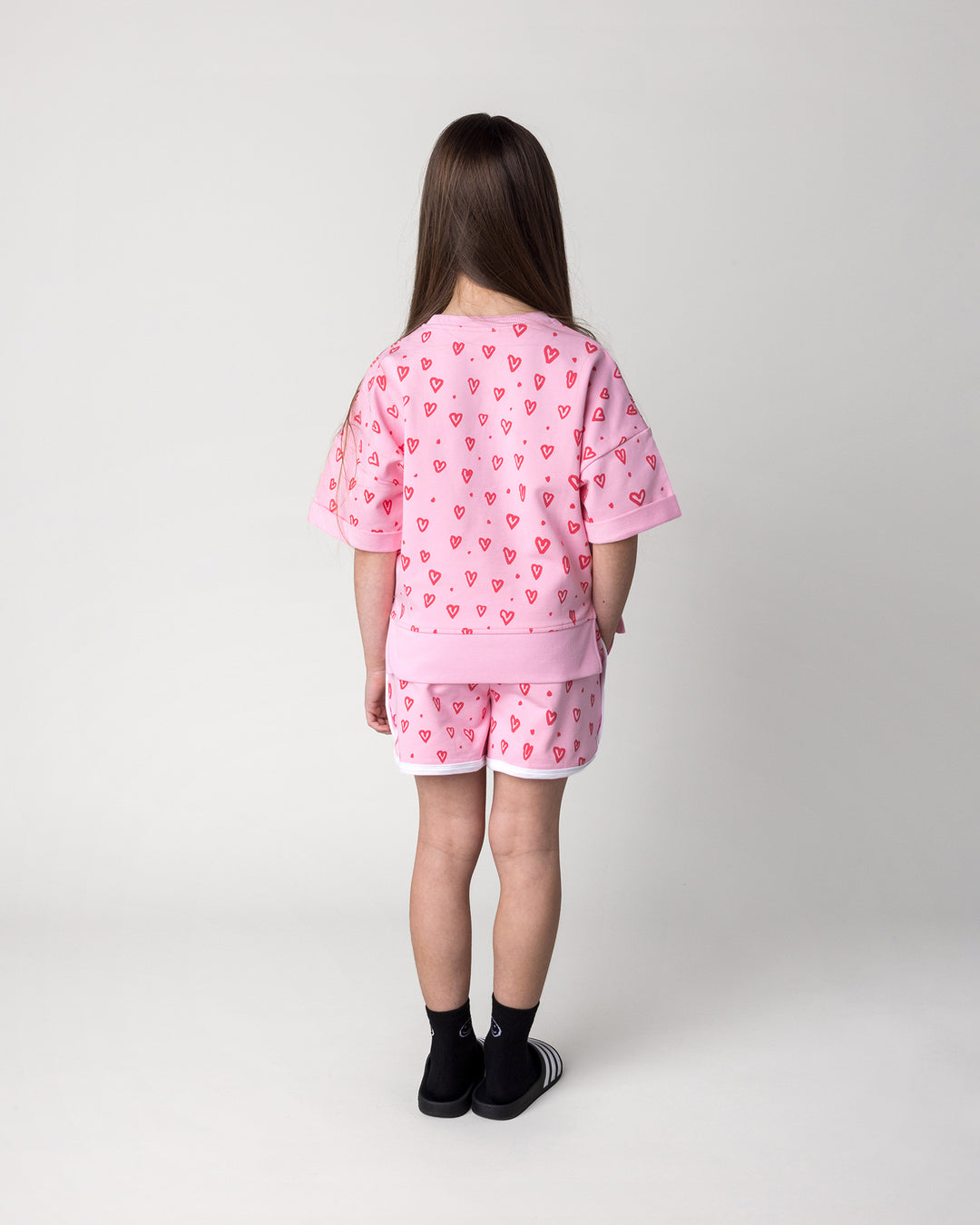 Kid wearing the Hearts Short in pink and white with the Hearts Short Sleeve Crew in pink, back view