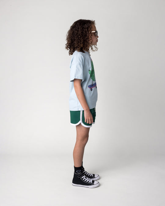 Kid wearing the Sprint Short in kelly green and white with the Skate Cactus Tee in light blue, side view