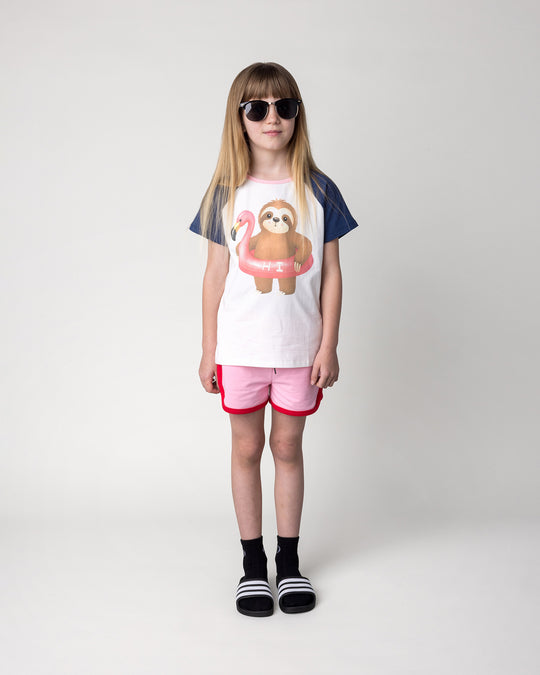 Kid wearing the Sprint Short in pink and red with the Swimming Sloth Tee in white, ink and pink, front view