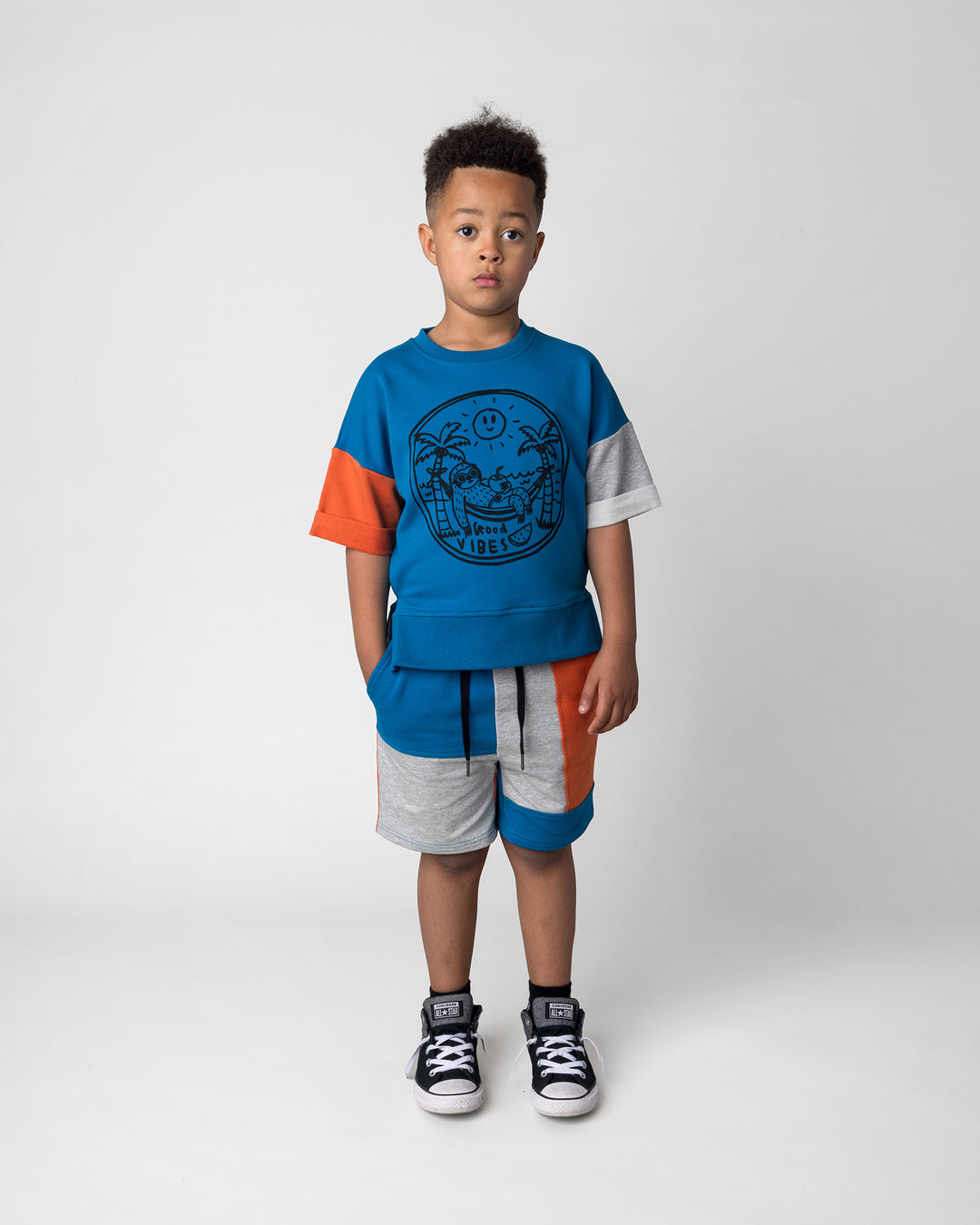 Kid wearing the Chill Sloth Short Sleeve Crew in teal, orange and grey marle with the Sliced Short in teal, orange and grey marle, front view