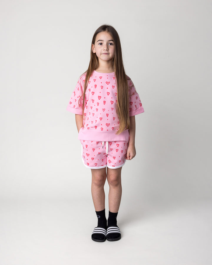 Kid wearing the Hearts Short Sleeve Crew in pink with the Hearts Short in pink and white, front view