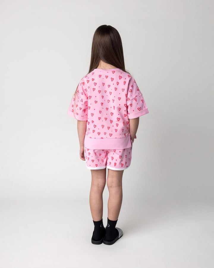 Kid wearing the Hearts Short Sleeve Crew in pink with the Hearts Short in pink and white, back view