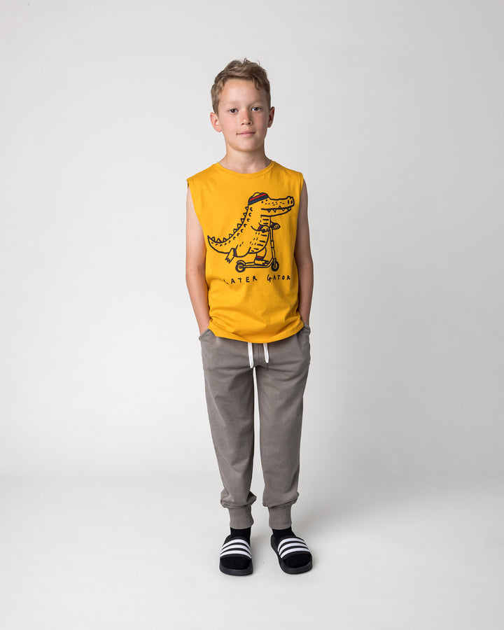 Kid wearing the Blasted Studio Trackies in grey wash with the Later Gator Sleeveless Tee in mustard, front view