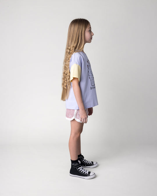 Kid wearing the Bear Hug Tee in lilac, lemon and blue with the Velvet Runner Short in blush and cream, side view