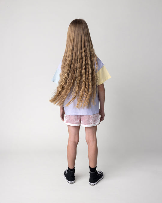 Kid wearing the Bear Hug Tee in lilac, lemon and blue with the Velvet Runner Short in blush and cream, back view