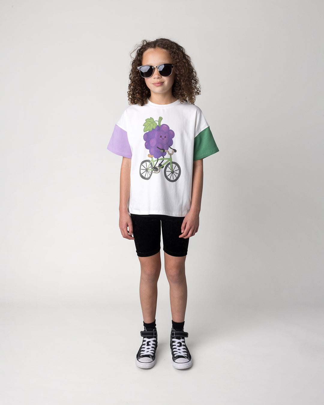 Kid wearing the Biking Grape Tee in white, purple and green with the Velvet Bike Pant in black, front view