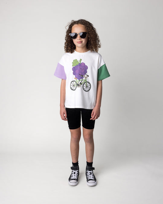 Kid wearing the Biking Grape Tee in white, purple and green with the Velvet Bike Pant in black, front view