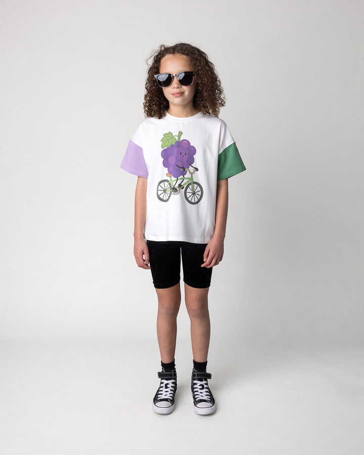 Kid wearing the Biking Grape Tee in white, purple and green with the Velvet Bike Pant in black, front view