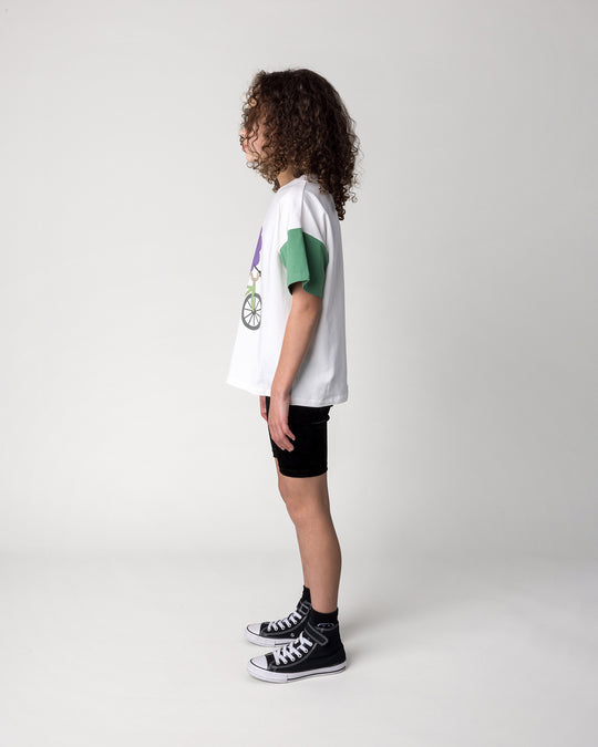 Kid wearing the Biking Grape Tee in white, purple and green with the Velvet Bike Pant in black, side view