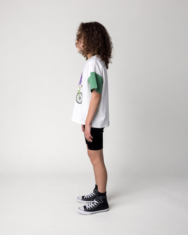 Kid wearing the Biking Grape Tee in white, purple and green with the Velvet Bike Pant in black, side view