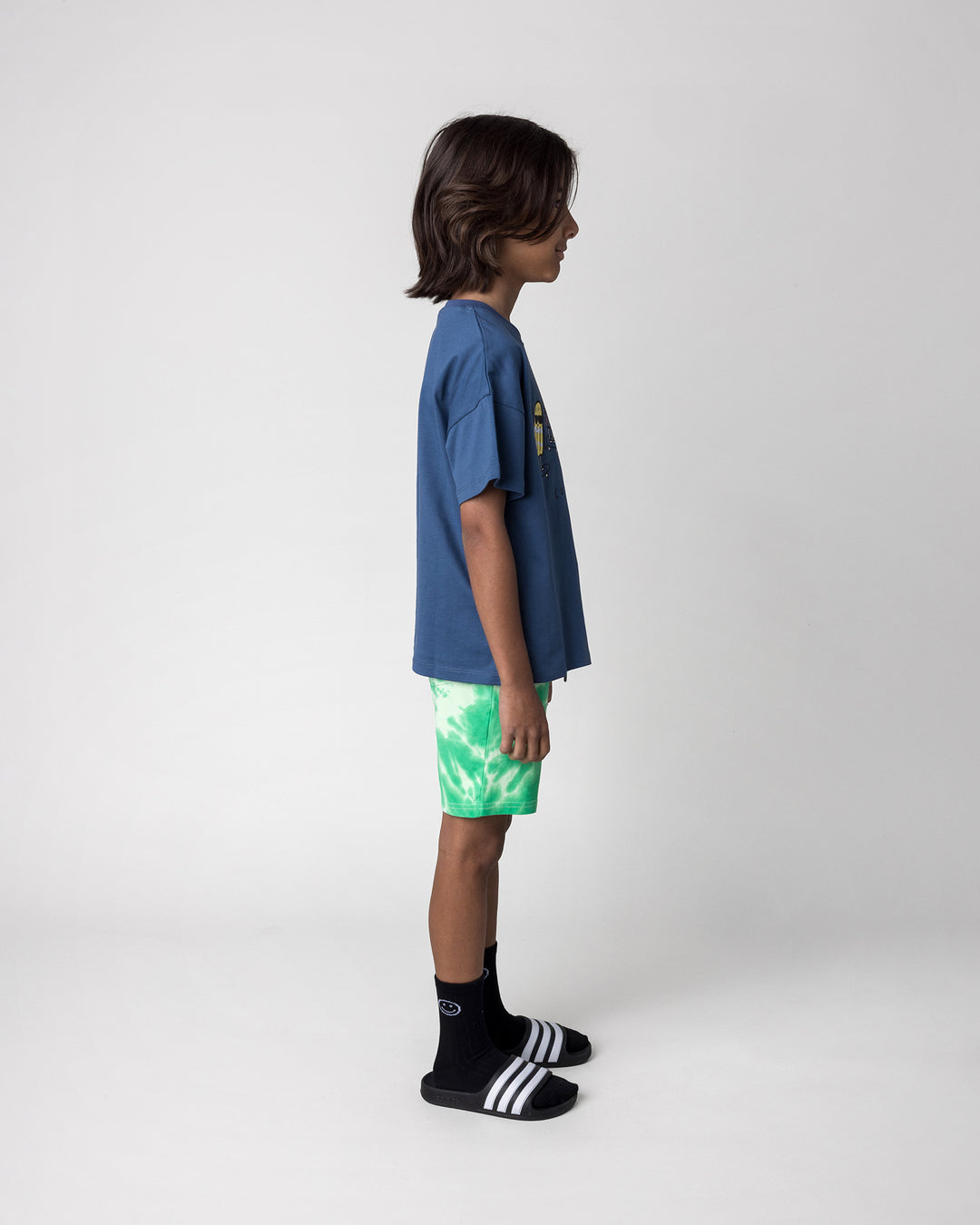 Kid wearing the Cool Crew Tee in blue with the Splatter Short in green, side view